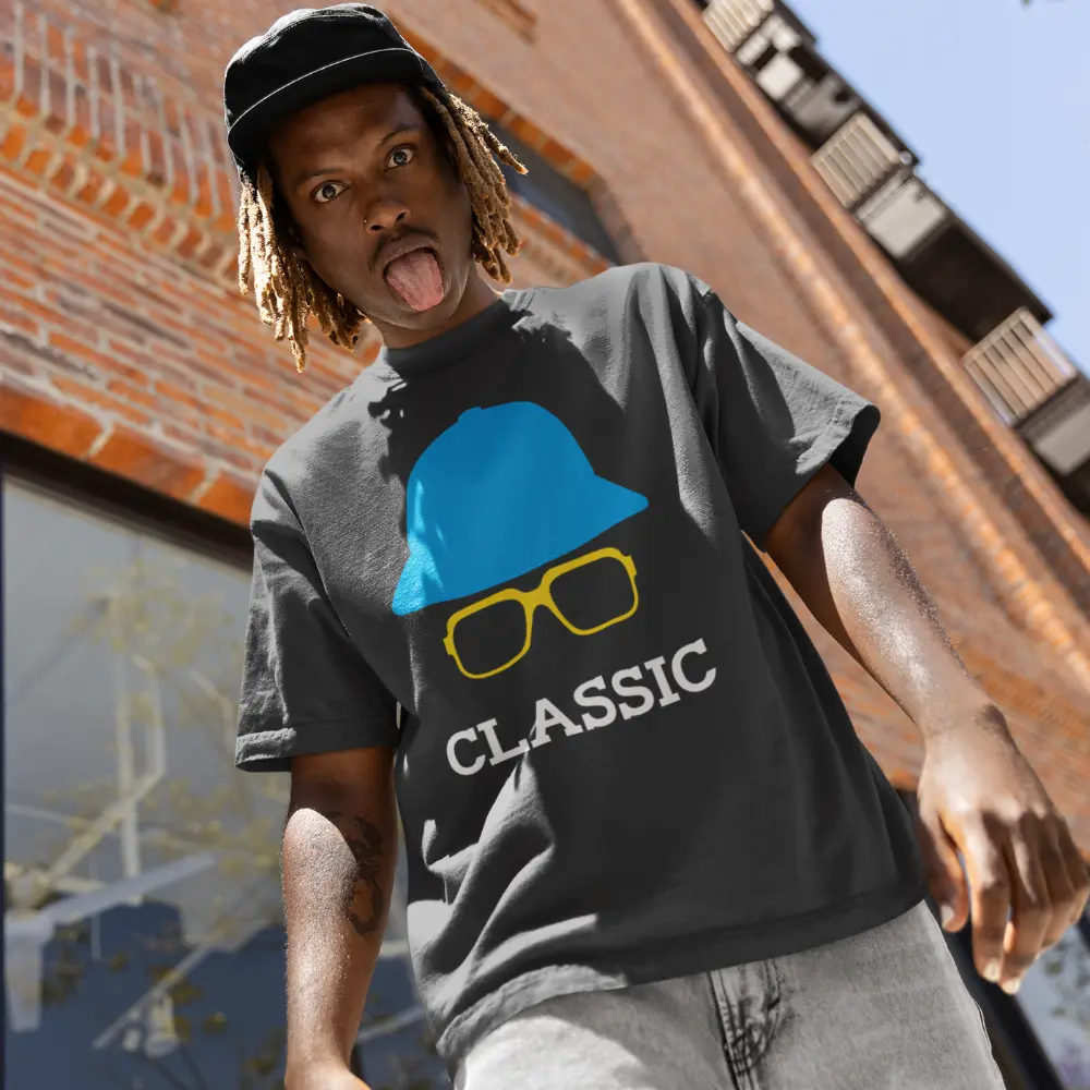 Man wearing a gray t-shirt with a blue hat, yellow glasses, and the word "CLASSIC" printed on it, posing playfully outdoors.