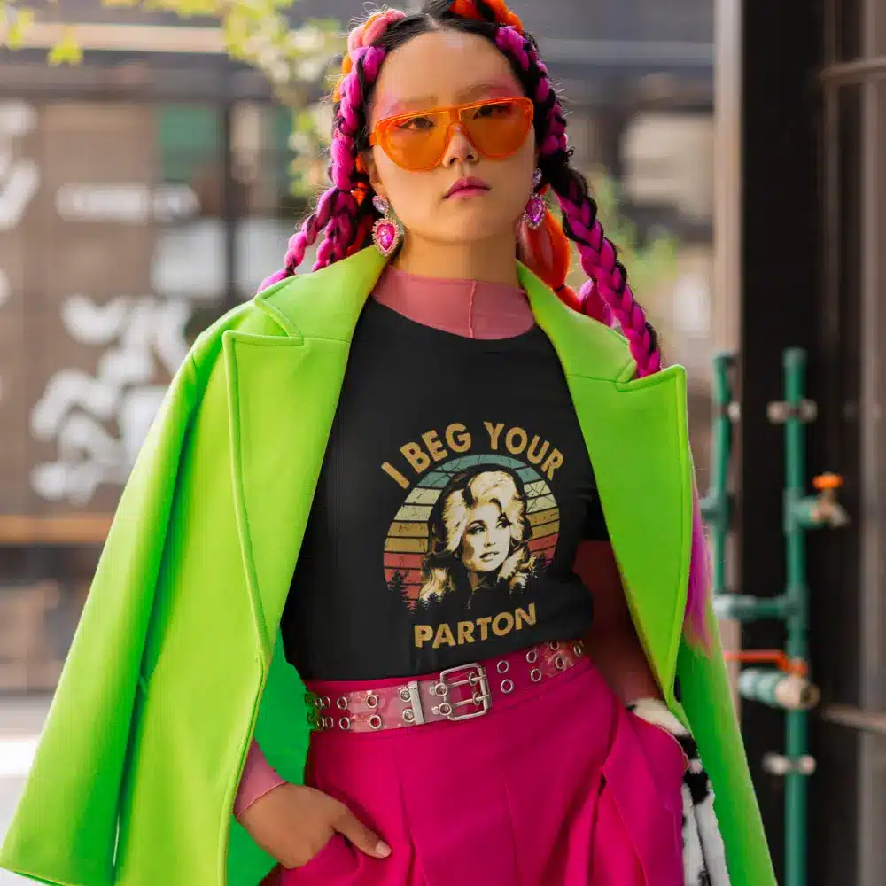 Person wearing a black t-shirt with the text "I Beg Your Parton" and an image of Dolly Parton, styled in bright clothing.