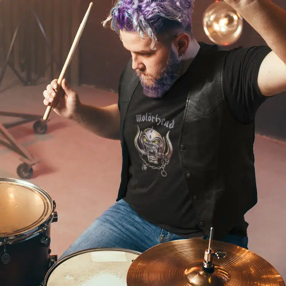 Person playing drums while wearing a black Motörhead t-shirt and a leather vest.