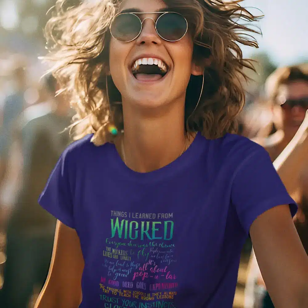 Woman wearing a purple t-shirt with text inspired by the musical "Wicked," smiling outdoors.