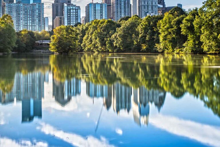 Piedmont Park lake reflecting Atlanta’s skyline, trees, and blue sky.
