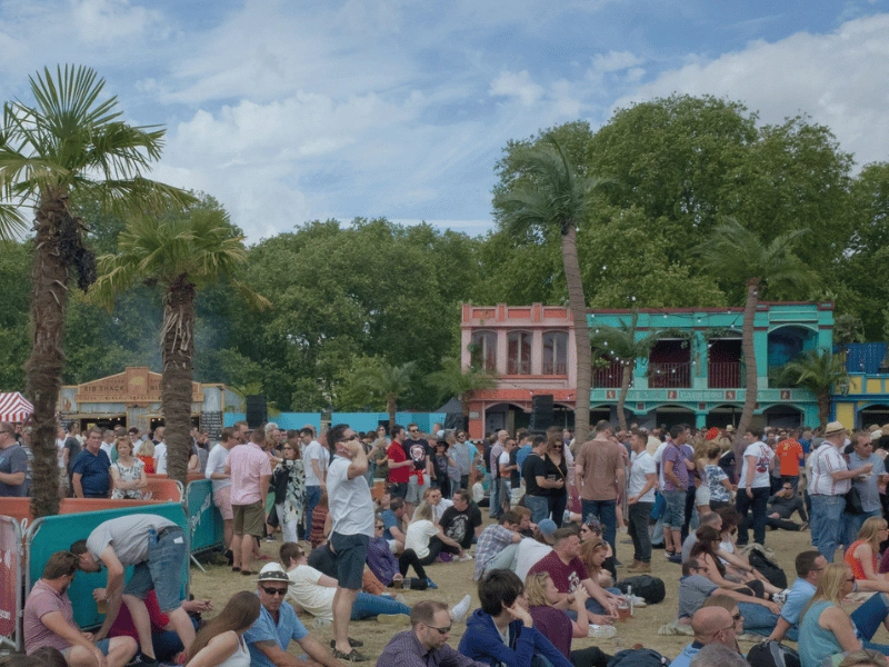 Festivalgoers relaxing on the grass among palm trees and colourful structures at BST Hyde Park.