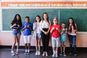 A teacher and her class posing in front of the chalkboard and used to represent the OTL Seat Fillers Denver teacher discount