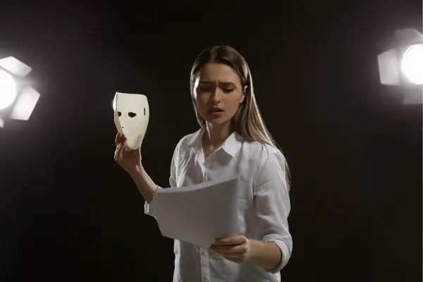 An actress rehearsing with a script in hand and a white mask, standing under a spotlight, illustrating an audition setting.