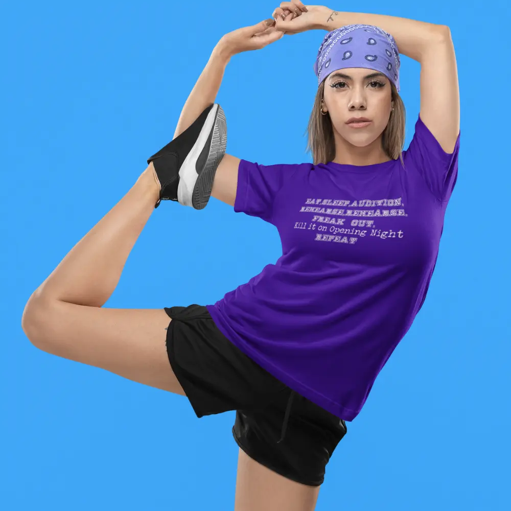 Person performing a dance stretch while wearing a purple t-shirt with the text "EAT. SLEEP. AUDITION. REHEARSE. REHEARSE. REHEARSE. FREAK OUT. Kill it on Opening Night. REPEAT.