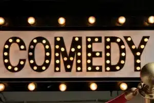 Comedy shows in the US and UK – A lit-up comedy club marquee sign with bright bulbs, creating a classic, inviting atmosphere for stand-up and improv performances