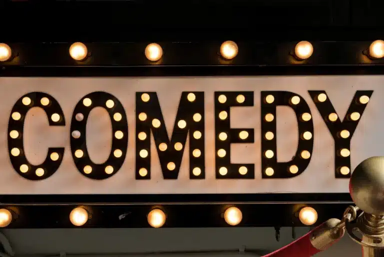 Comedy shows in the US and UK – A lit-up comedy club marquee sign with bright bulbs, creating a classic, inviting atmosphere for stand-up and improv performances