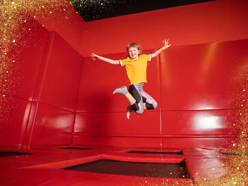 Child jumping mid-air in a bright red trampoline park, wearing a yellow shirt and grip socks—capturing the fun of indoor adventure memberships.