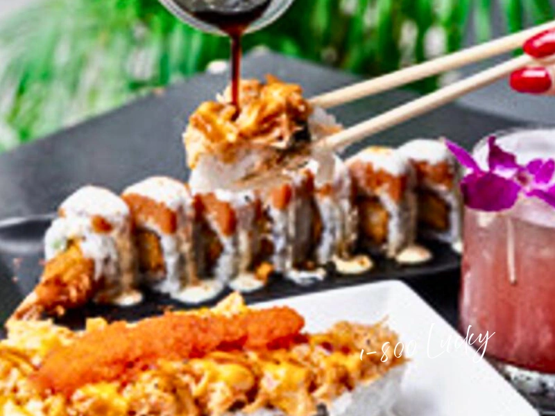 Chopsticks lifting sushi roll at 1-800-Lucky with sauce drizzle and cocktail, South Florida foodie gift