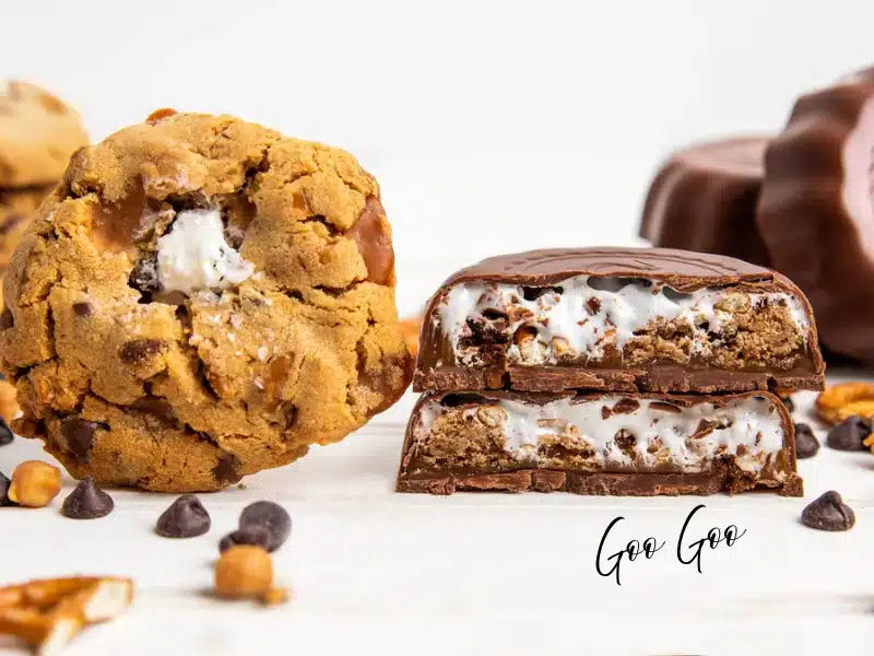 Goo Goo — Nashville’s classic candy — halved chocolate cluster showing marshmallow-nougat and crunchy bits beside a stuffed chocolate-chip cookie on white.