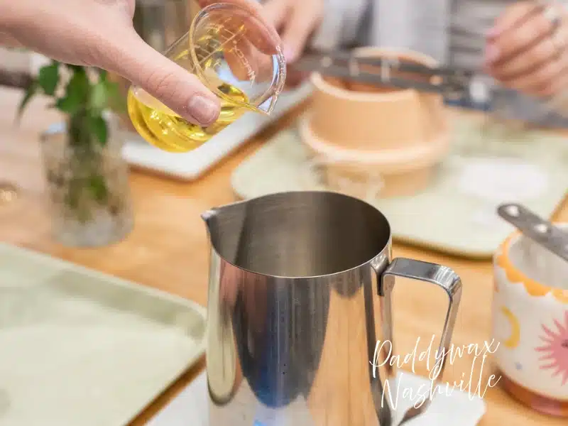 Pouring fragrance oil into a metal pitcher at Paddywax Candle Bar Nashville—DIY candle-making experience gift.