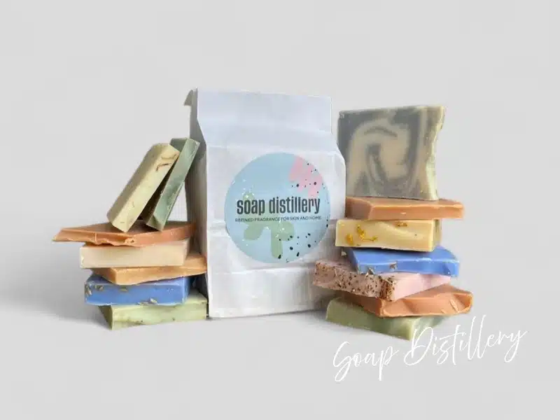 Colorful handmade soap bars stacked around a white “Soap Distillery” bag—Chicago-made bath & body gift.
