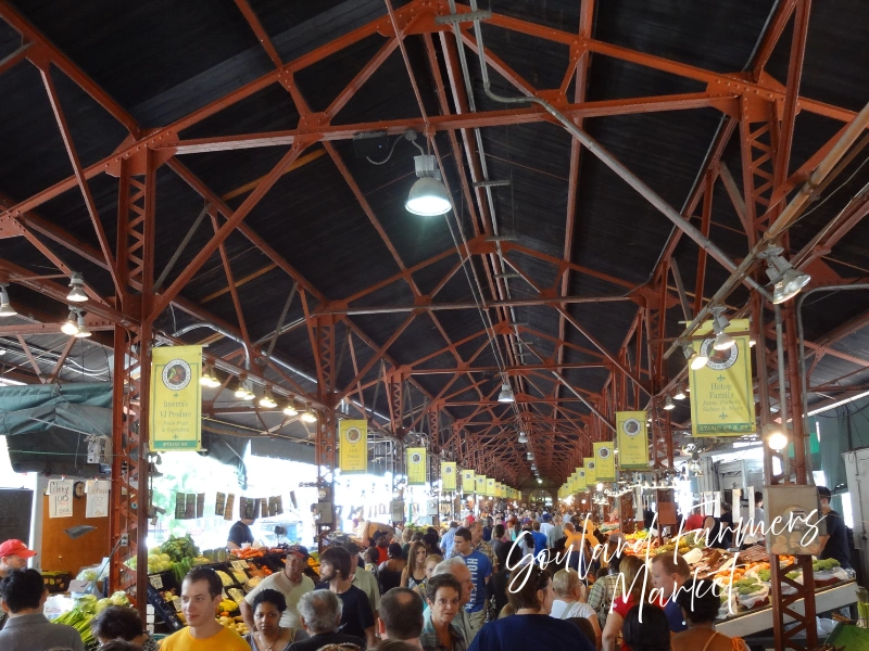 Crowds shopping produce stalls under the red iron canopy at Soulard Farmers Market, St. Louis