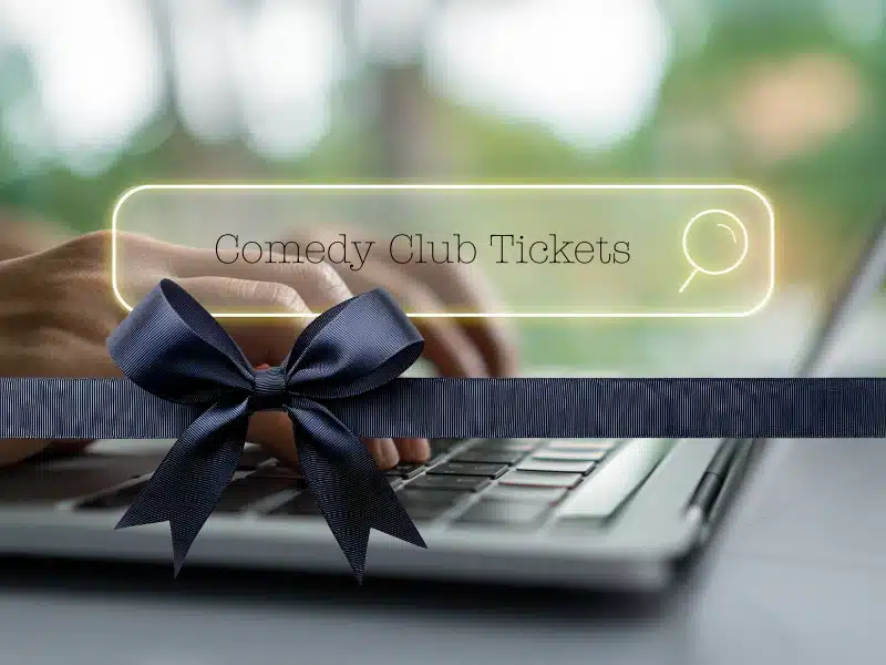 gift of experience search: hands on laptop with glowing “Comedy Club Tickets” search bar and navy bow