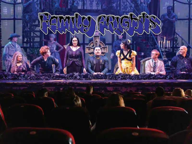 The scene is set with an array of addams family characters while families watch from theatre seats. Morticia adams and gomez adams are pleased under funky text saying family frights. Dazzling set and background characters fill up the stage ensuring a fun night.