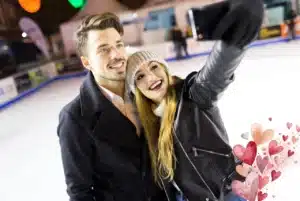 Budget-friendly things to do for Valentine’s Day: couple taking a selfie while ice skating, with watercolor heart accents.