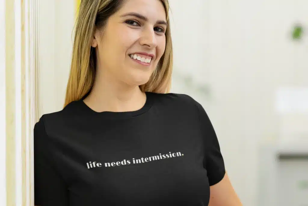 Woman modeling a black “life needs intermission.” t-shirt with white text and a small green period.