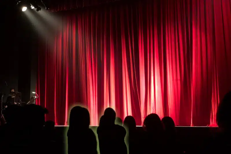 Theatre seats facing a stage before a live play, with warm stage lighting.