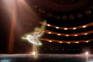 Ballet dancer performing on a grand theatre stage under dramatic spotlights.