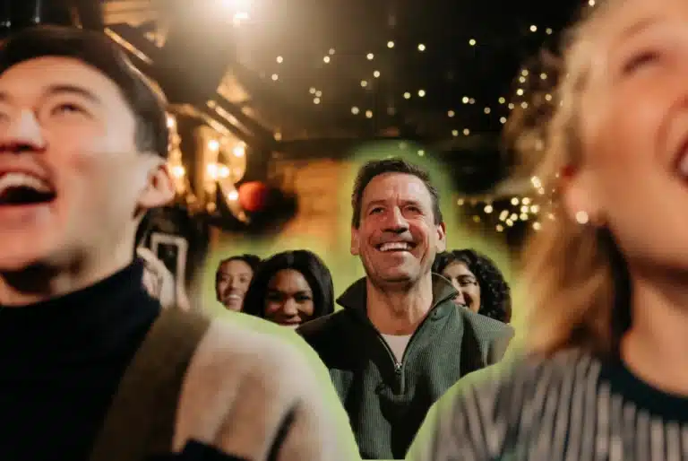 Audience laughing at a live comedy show in a warmly lit club, with smiling guests facing the stage.
