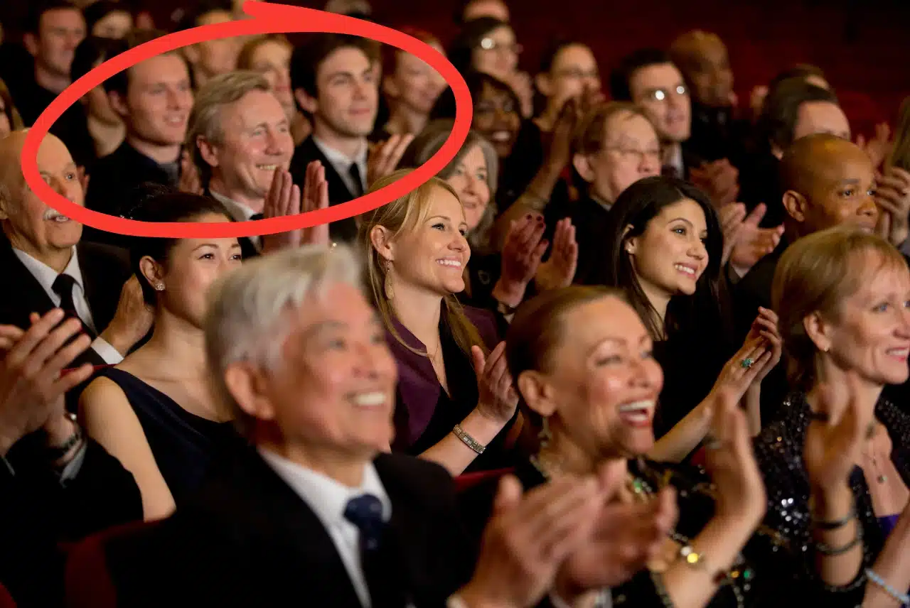 Theatre audience applauding during a live performance, with several guests seated together in the crowd.