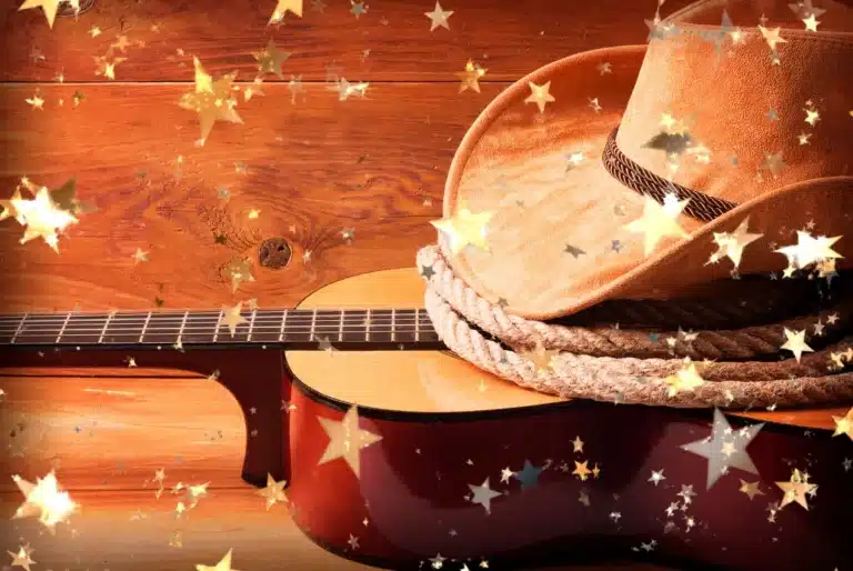 Cowboy hat and acoustic guitar on a warm wood background with glowing star confetti.
