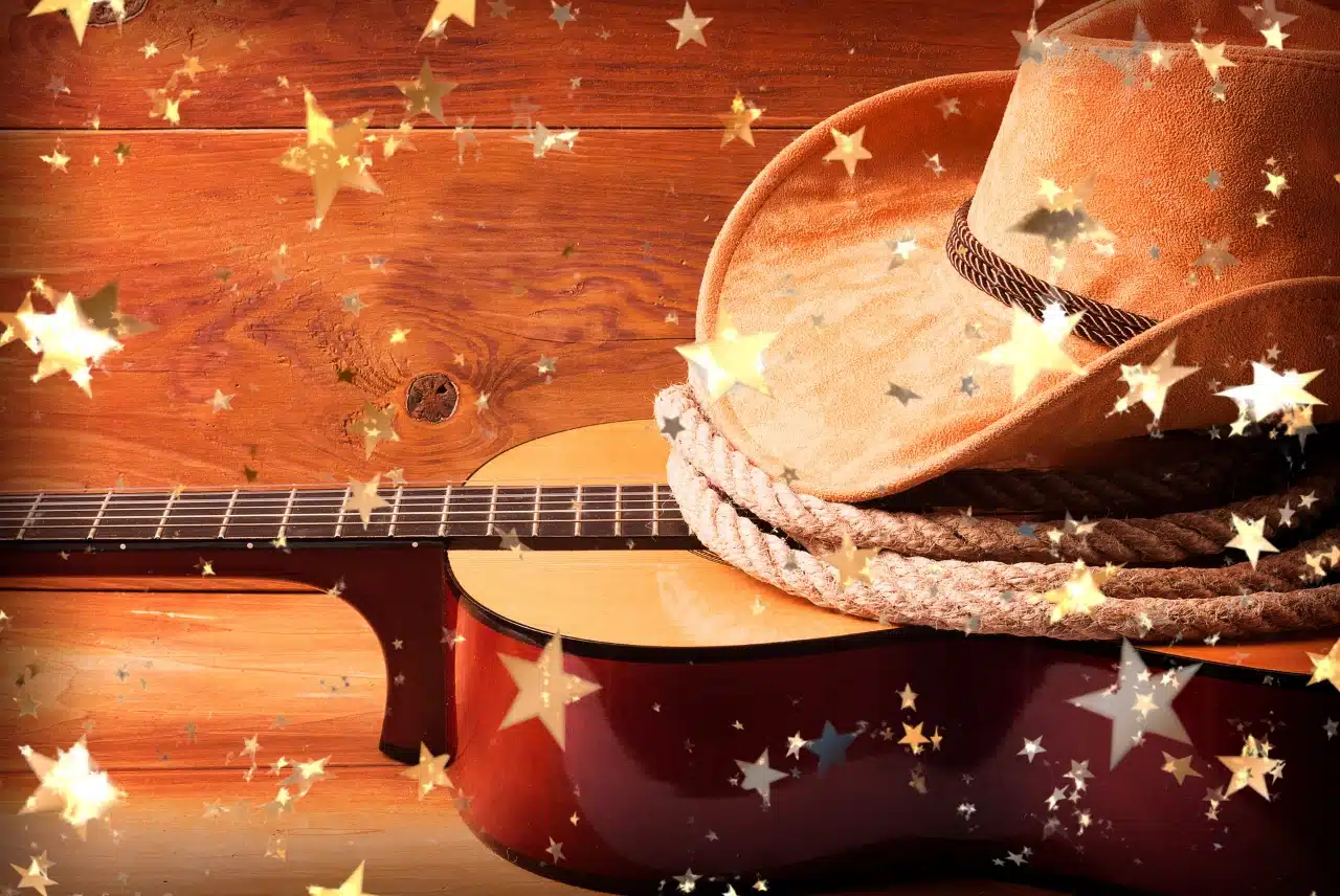 Cowboy hat and acoustic guitar on a warm wood background with glowing star confetti.