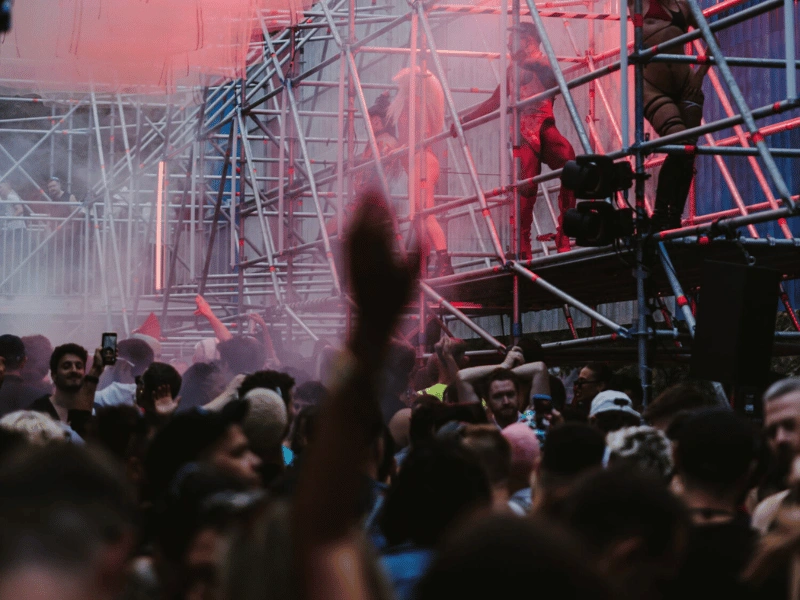 Festivalgoers dancing beneath red lighting and industrial stage scaffolding at Body Movements.