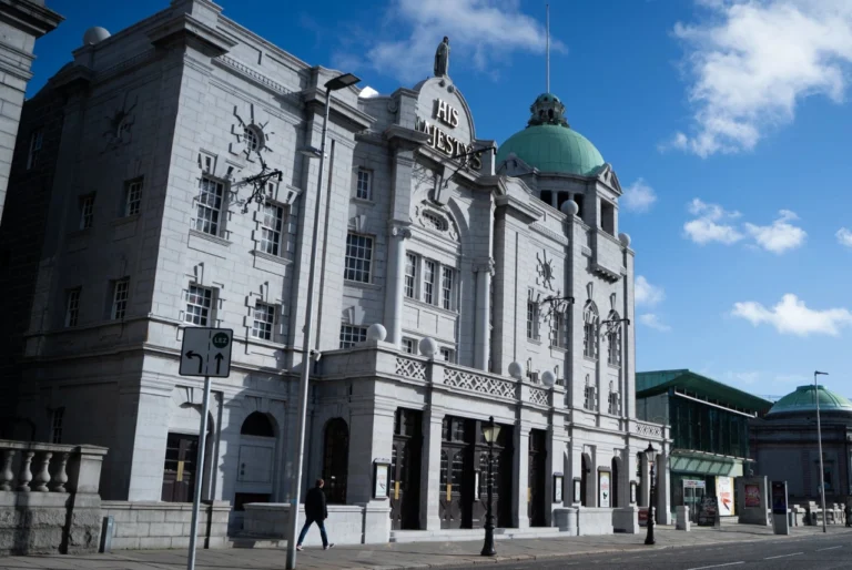 Historic granite façade of His Majesty’s Theatre on Rosemount Viaduct in Aberdeen, Scotland, beneath a blue sky.