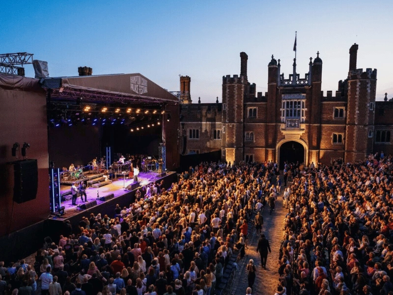 An evening concert stage and seated audience inside the historic courtyard at Hampton Court Palace Festival.